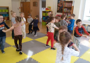 Widok na salę przedszkolną i grupę tańczących w parach dzieci.